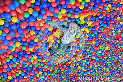 Happy little girl lays on the big heap of multicolored small balls Stock Photo