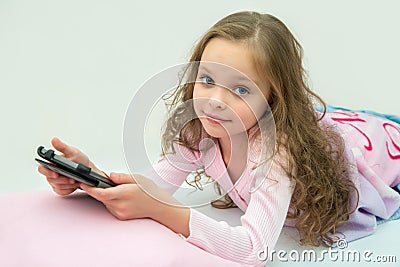 Happy little girl lying on bed with tablet computer Stock Photo