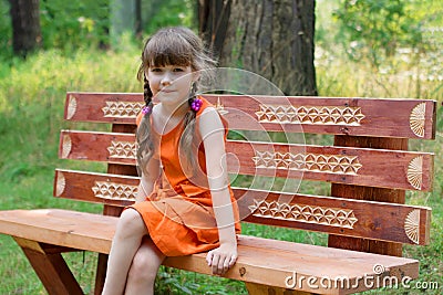 Happy little girl in orange sits on wooden beanch at summer Stock Photo