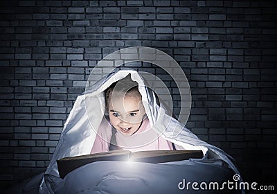 Happy little girl reading book in bed Stock Photo