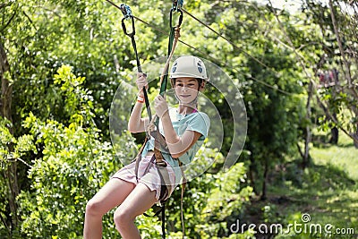 Happy little girl riding a zip line in a lush tropical forest Stock Photo