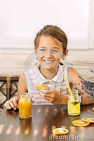 Happy little girl of school age enjoying healthy breakfast eating sandwich and fruits and drinking orange juice sitting Stock Photo