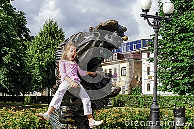 Happy little girl sitting on bronze sculpture of clown Stock Photo