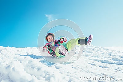 Happy little girl slides down from the snow slope. Enjoying the Stock Photo