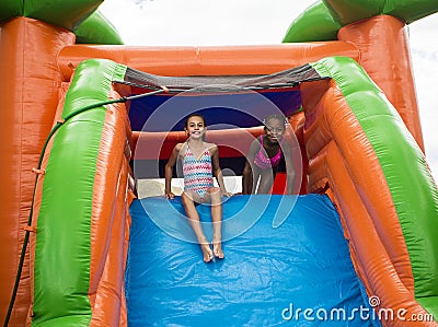 Happy little girls sliding down an inflatable bounce house Stock Photo