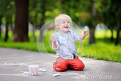 Happy little kid boy drawing with colored chalk on asphalt. Stock Photo