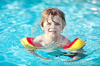 Happy little kid boy having fun in an swimming pool. Active happy preschool child learning to swim. with safe floaties Stock Photo