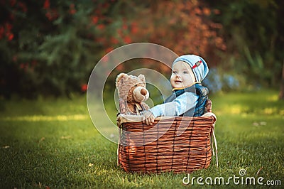 Happy little kid boy playing with bear toy while sitting in basket on green autumn lawn. Children enjoying activity outdoor. Stock Photo