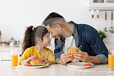 Happy Loving Arab Dad And Daughter Eating Sandwiches In Kitchen And Bonding Stock Photo