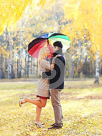 Happy loving couple hugging with colorful umbrella together in warm sunny day over yellow flying leafs Stock Photo