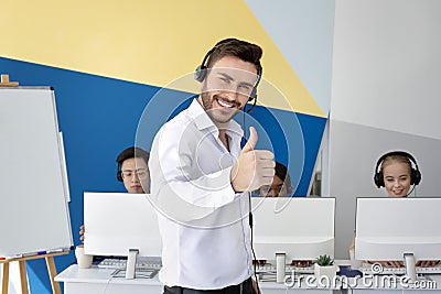 Happy male hotline operator smiling and showing thumb up gesture at modern open space office Stock Photo