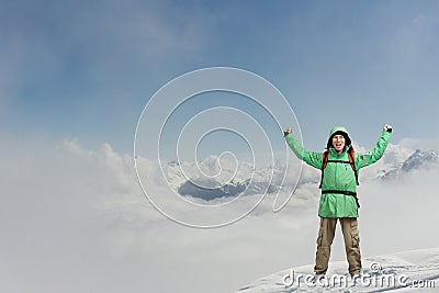 Happy male mountaineer man with raised arms. In background high mountains above clouds . Stock Photo