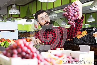 Happy male seller offering grapes in shop Stock Photo