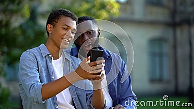 Happy male teenager showing smartphone application to father sitting outdoors Stock Photo