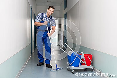 Happy male worker with broom cleaning office corridor Stock Photo