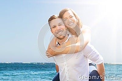 Happy Man Giving Piggyback To His Wife At Beach Stock Photo