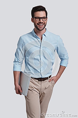 Happy man. Good looking young man carrying laptop and looking a Stock Photo