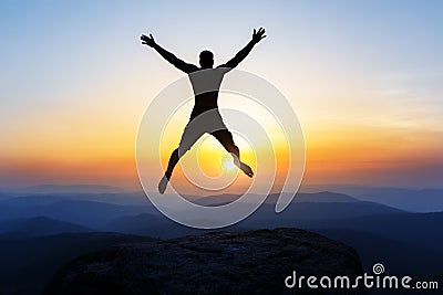 Happy man jumping for joy on the peak of the mountain, cliff at sunset. Success, winner, happiness Stock Photo