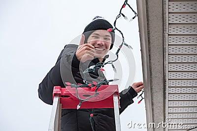 Man climbing a ladder to hang christmas lights outdoors. Stock Photo