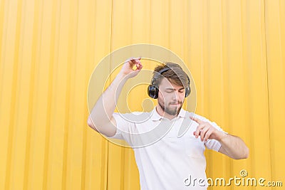 Happy man listens to music on headphones and smiles on the background of a yellow wall Stock Photo