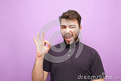 Happy man on a purple background smiles at the sign OK. Bearded man shows what he likes, looks at the camera, isolated on a purple Stock Photo