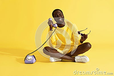 Happy man talking on purple phone sitting on yellow background Stock Photo