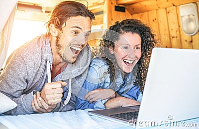 Happy man and woman watching surprised on their computer - Travel couple using laptop during their journey on a vintage minivan Stock Photo