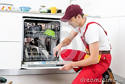 Happy master. Male technician sitting near dishwasher with screwdriver in kitchen with instruments and smiling Stock Photo