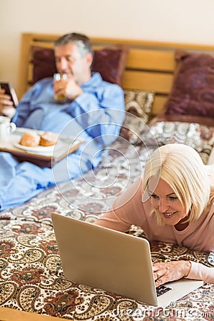 Happy mature blonde using laptop on bed Stock Photo