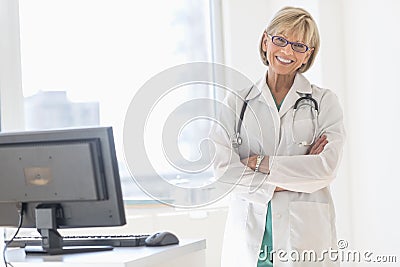 Happy Mature Female Doctor Standing Arms Crossed In Hospital Stock Photo