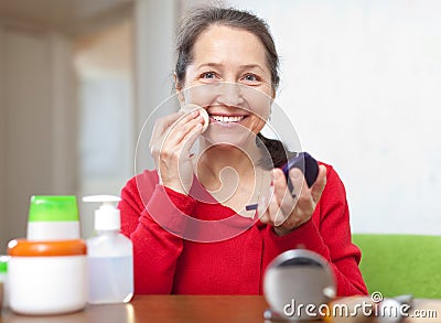 Happy mature woman puts facepowder Stock Photo