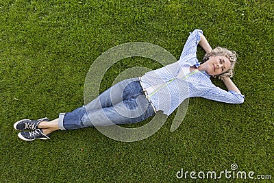 Happy middle-aged woman in casual weekend clothing relaxing on the grass in a park Stock Photo