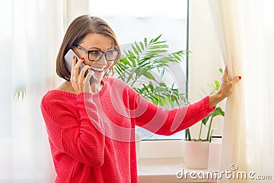 Happy middle aged woman female talking on mobile cell phone. Background window in the house. Stock Photo