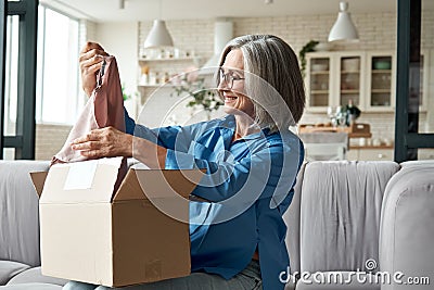 Happy middle aged woman opening parcel unpacking postal delivery box at home. Stock Photo