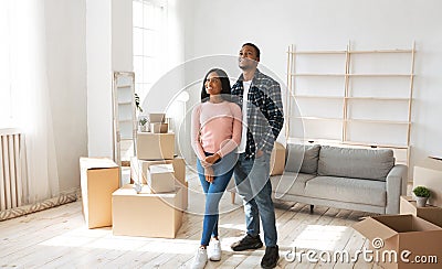 Happy millennial black couple standing in their new house among cardboard boxes on moving day Stock Photo