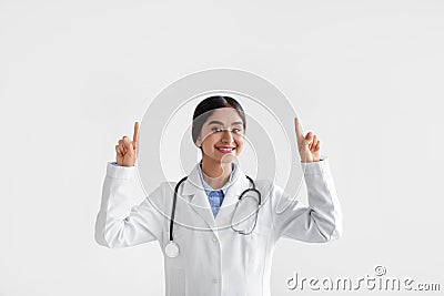 Happy millennial indian lady doctor in coat with phonendoscope raises hands and shows fingers up Stock Photo