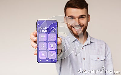 Happy millennial man showing mobile phone with smarthome automation control system on screen, white background Stock Photo