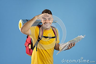 Happy millennial tourist with camping equipment and map looking at camera on blue studio background Stock Photo