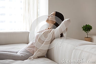 Happy millennial woman relaxing on sofa, breathing cool air Stock Photo
