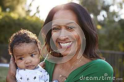 Happy African American middle aged grandmother holding her three month old grandson in the garden and smiling to camera, close up Stock Photo