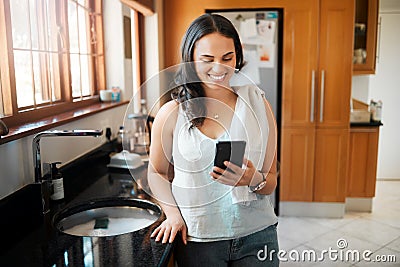 Happy mixed race woman smiling while using smart phone at home. Woman reading text message or chatting on social media Stock Photo