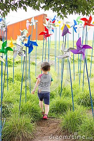 Happy Mixed raced Boy running to grass though wind spinners Stock Photo