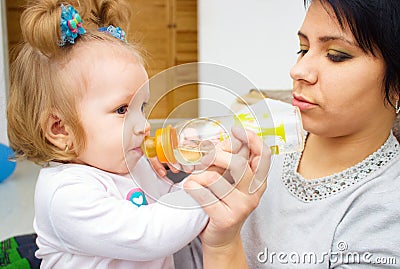 Happy mom and baby girl drinking from bottle. The concept of childhood and family. Beautiful Mother and her baby Stock Photo