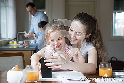 Happy mom and daughter playing game on smartphone together Stock Photo