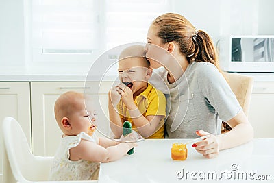 Happy mom spends time with the children in the kitchen feeding them. Stock Photo