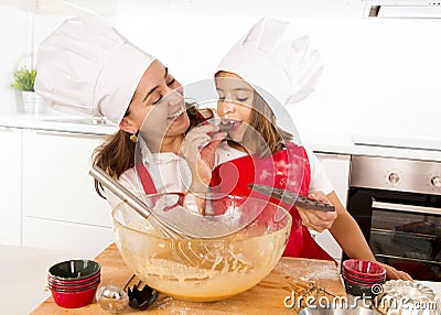 Happy mother baking with little daughter eating chocolate bar used as ingredient while teaching the kid Stock Photo