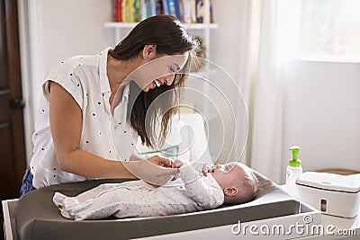 Happy mother changing the diaper of her newborn son at home on a baby changing table, waist up Stock Photo