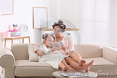 Happy mother and daughter with curlers and phone on sofa at home Stock Photo