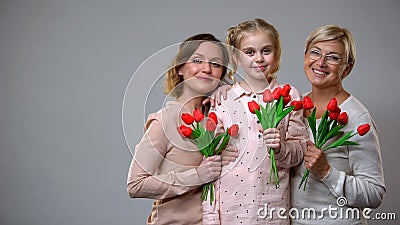 Happy mother, daughter and granny holding tulips grey background, spring holiday Stock Photo