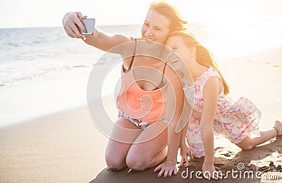 Happy mother and daughter taking selfie photo with smartphone on the beach - Mother having fun with her kid on holiday vacation - Stock Photo